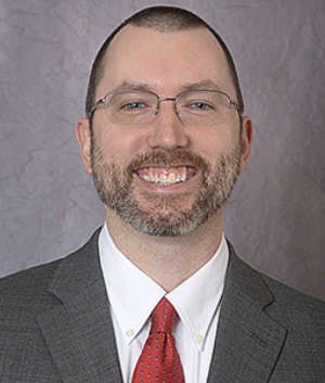 Portrait of Kevin Brock. He is dressed in a suit and tie and is smiling at the camera.